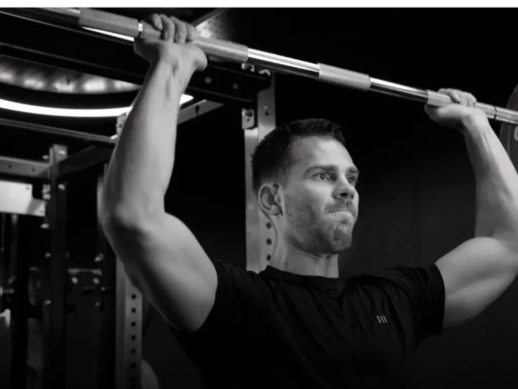 Male performing barbell shoulder press during personal training session in London gym – strength training, fitness transformation, and online personal trainer services.