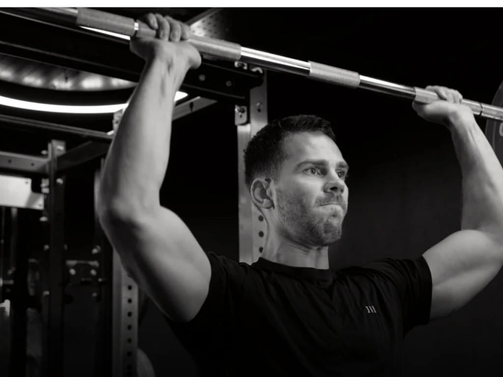 Male athlete performing barbell shoulder press at a London gym – strength training, muscle building, and fitness transformation guided by a professional personal trainer.